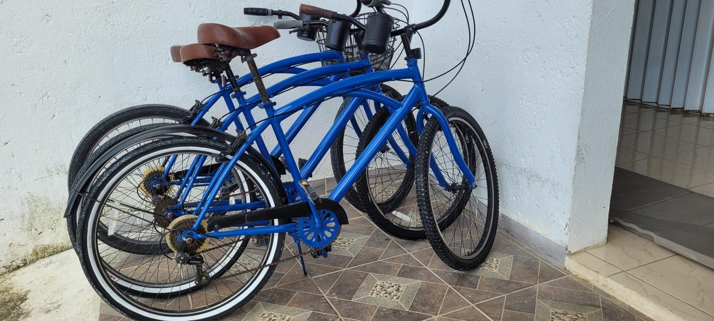 Ein blaues Fahrrad mit braunem Sattel und schwarzen Reifen, geparkt an einer weißen Wand auf einem gefliesten Boden.