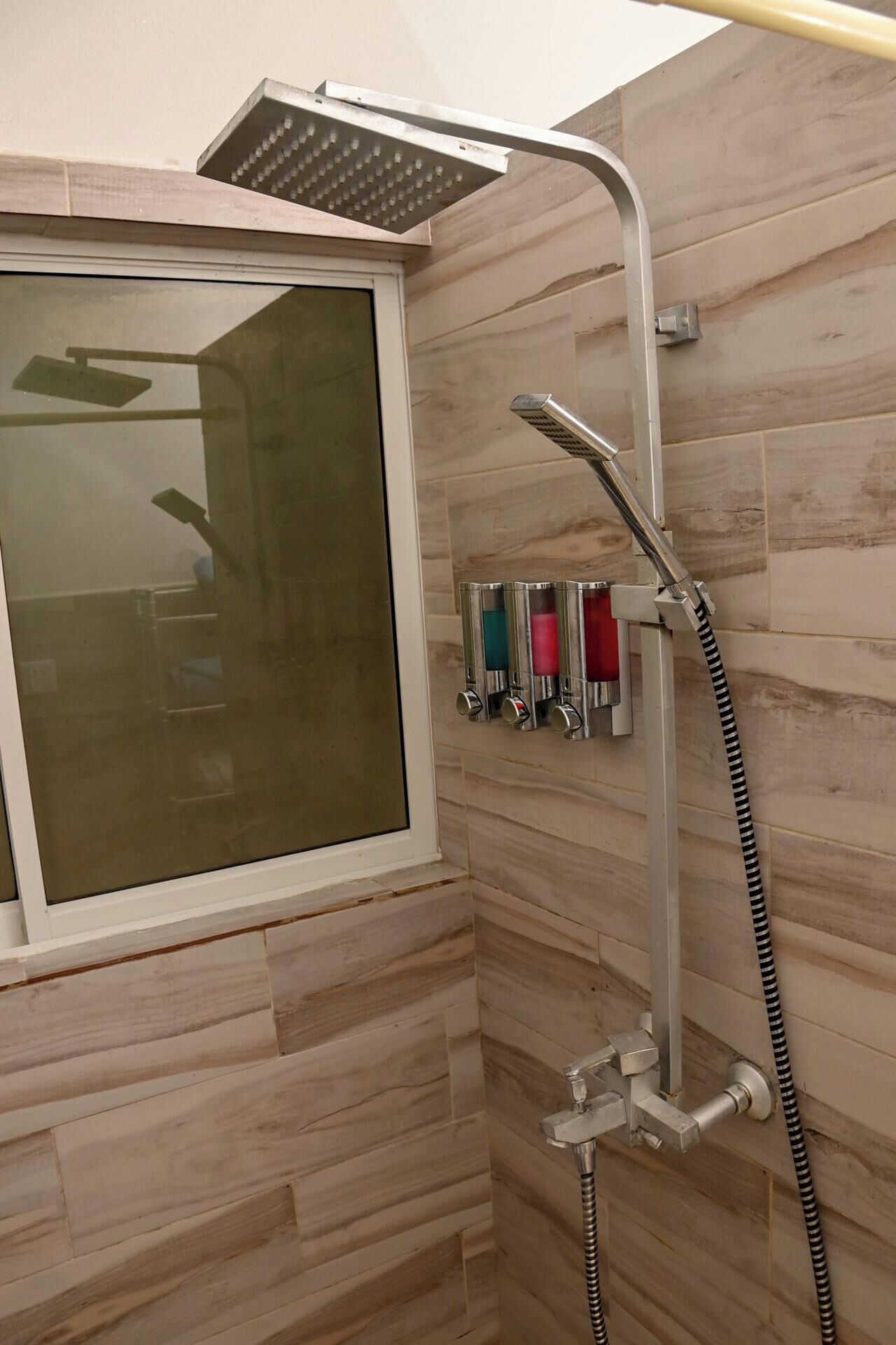 A shower area with a window, a handheld showerhead, and a wall-mounted faucet.