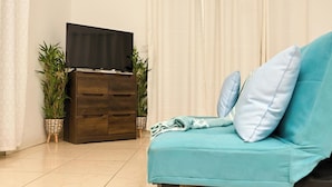 Una sala de estar con un sofá color turquesa, un mueble de madera oscura con un televisor de pantalla plana y dos plantas en macetas.