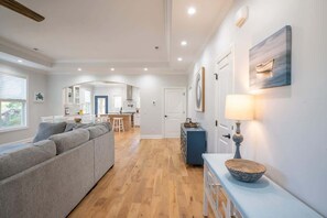 A modern living room with a sofa, a dining area with a table and chairs, and a kitchen in the background.