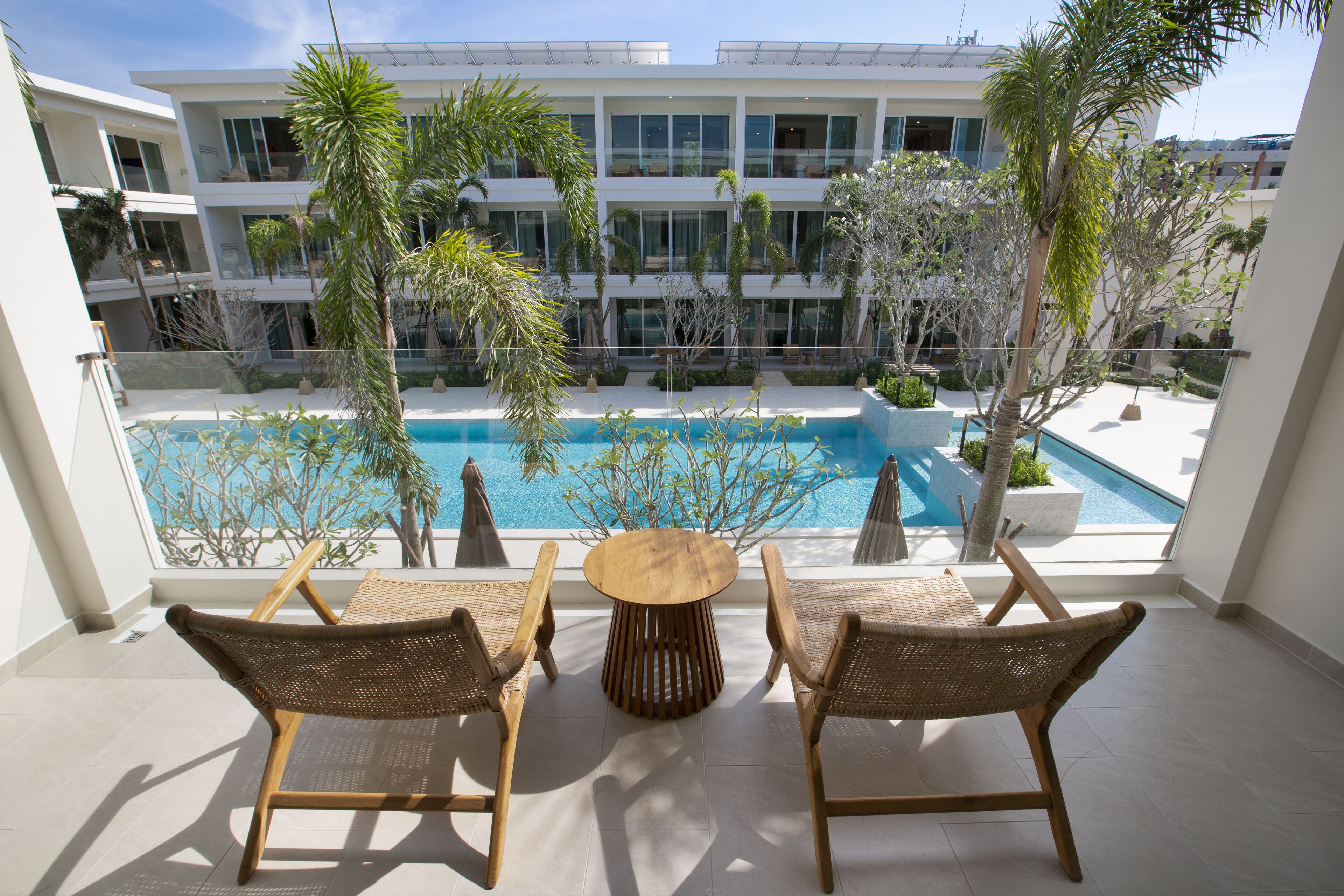 A balcony with a view of a swimming pool, wicker chairs, and a round table.