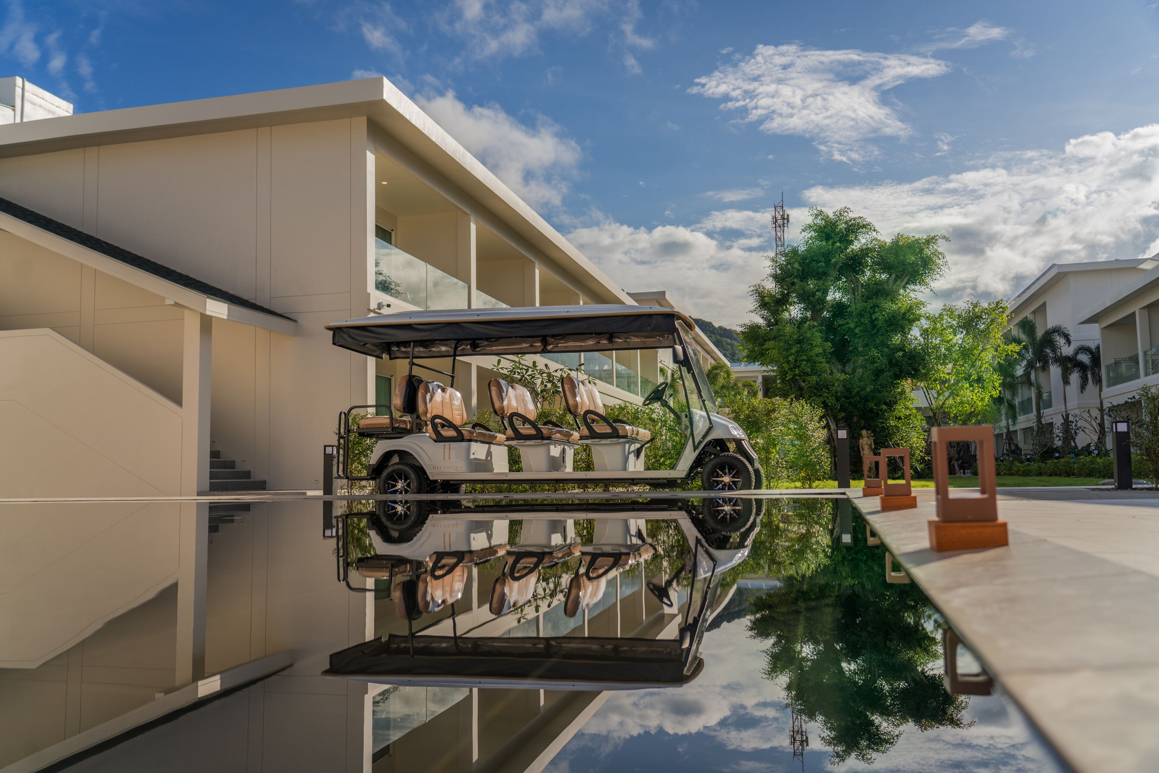 Ein modernes Gebäude mit einem spiegelnden Pool, ein weißer SUV davor und ein klarer Himmel.