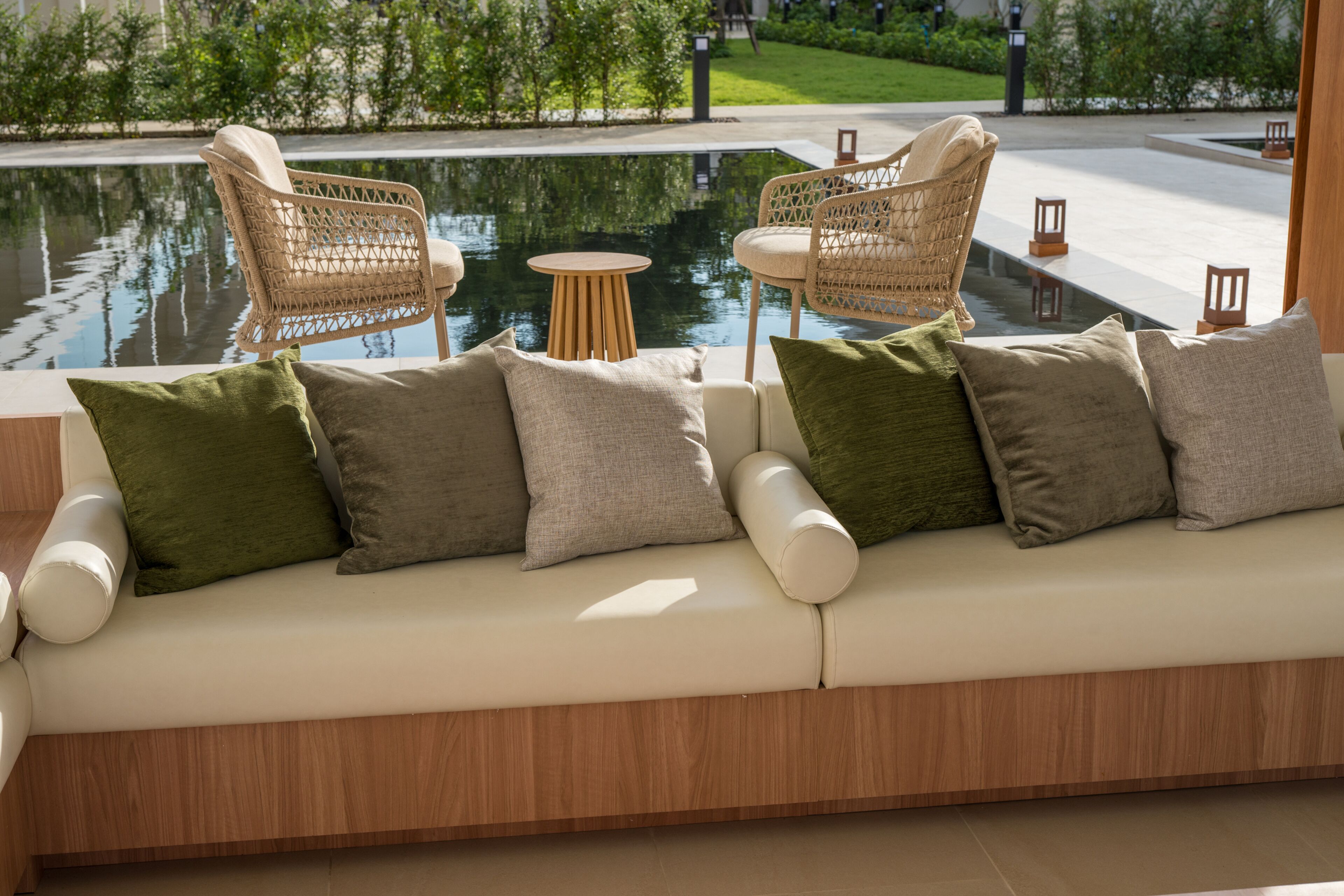 Un área de estar al aire libre moderna con piscina, sillas de mimbre, una mesa redonda y un sofá con cojines.