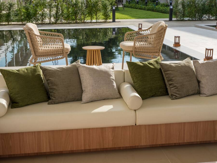 Un área de estar al aire libre moderna con piscina, sillas de mimbre, una mesa redonda y un sofá con cojines.