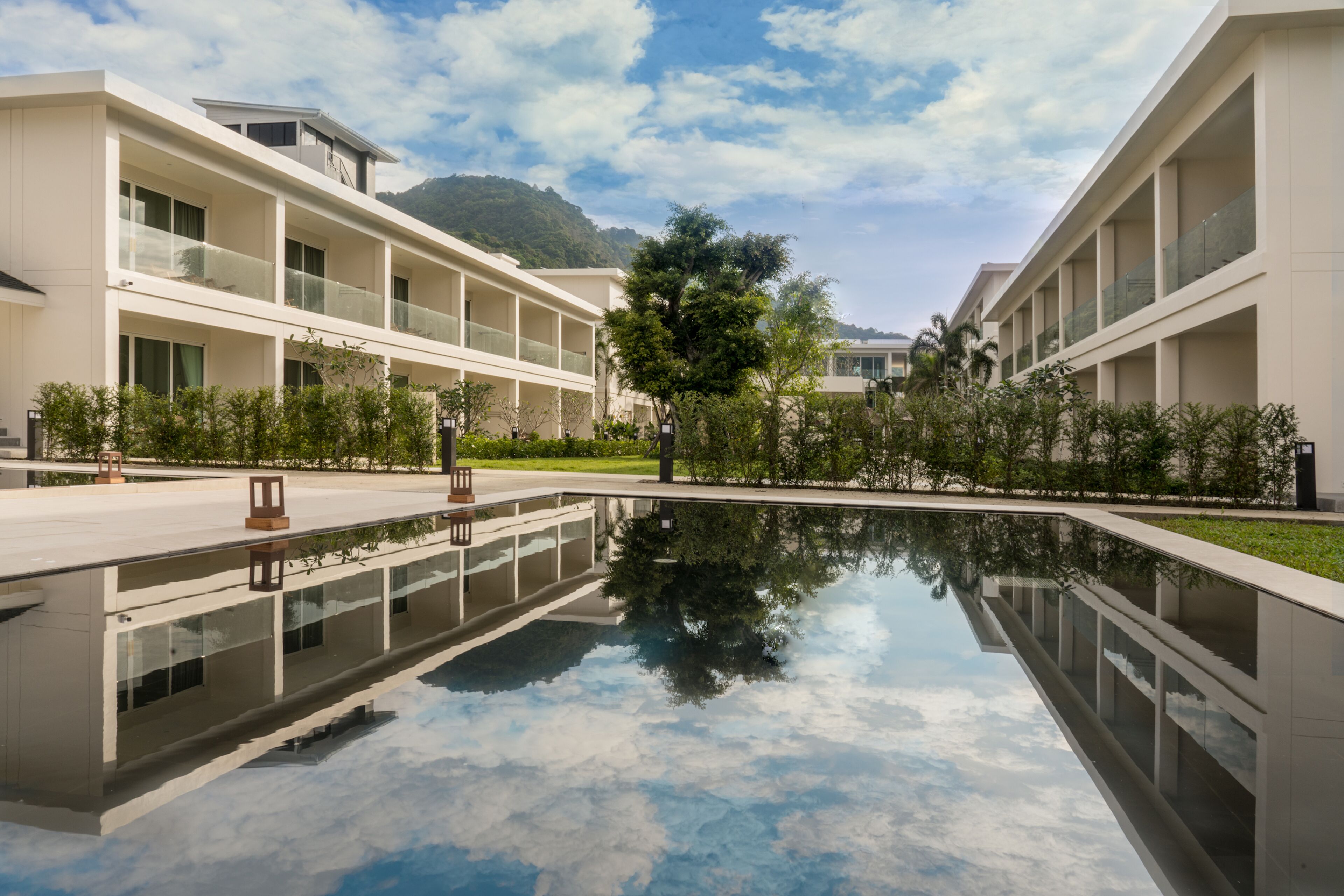 Un bâtiment moderne doté d’un bassin aux reflets changeants, entouré de verdure et avec une montagne en toile de fond.