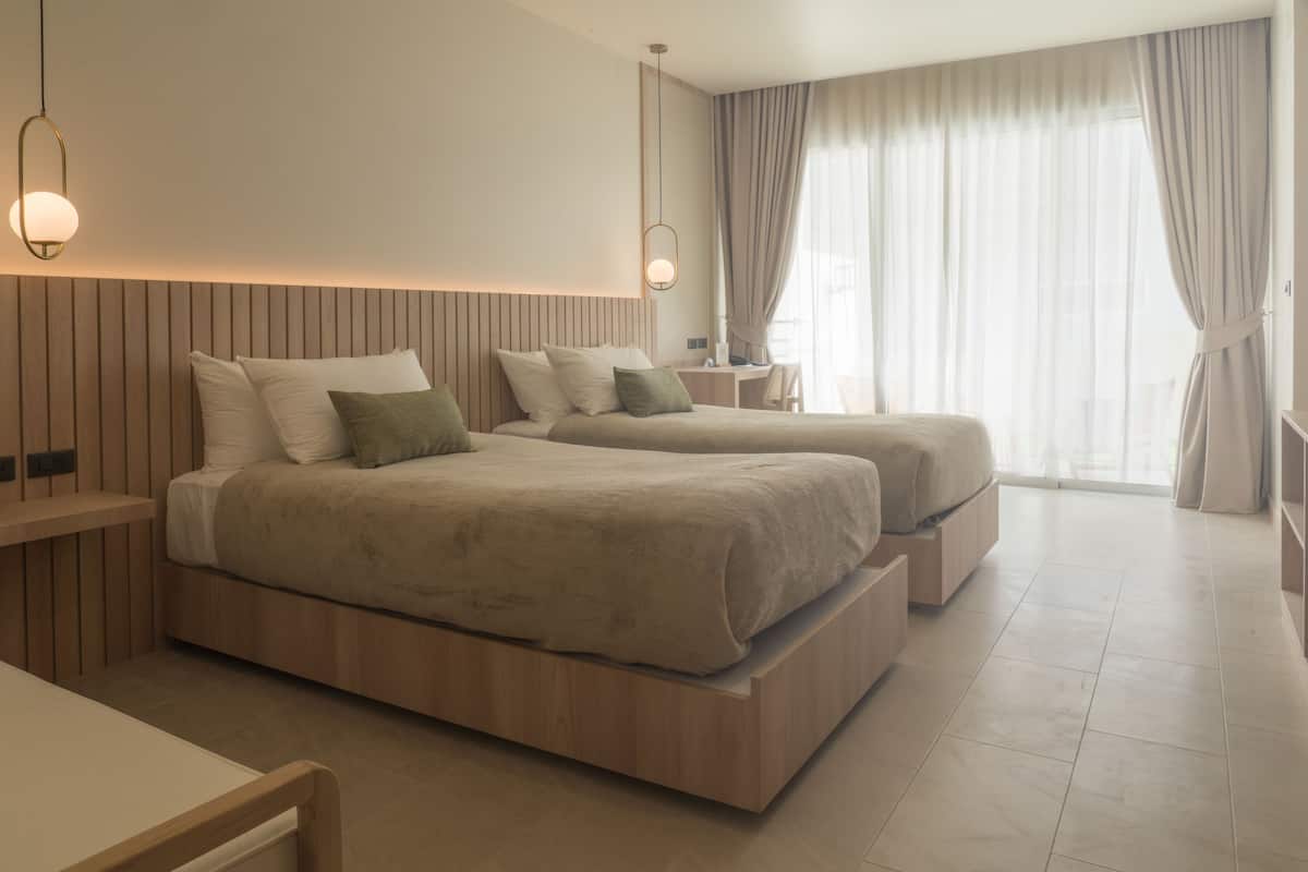 Una habitación de hotel moderna con dos camas, un escritorio y un ventanal con cortinas.
