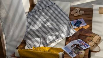 Une pièce baignée de lumière, avec un lit, une table en bois sur laquelle repose un magazine, une paire de chaussons et une serviette enroulée.
