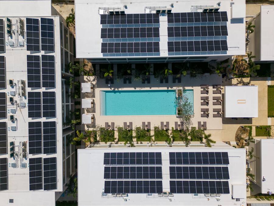 Vista aérea de un hotel con varios pisos, cada uno equipado con paneles solares, una piscina central y zonas de estar al aire libre.