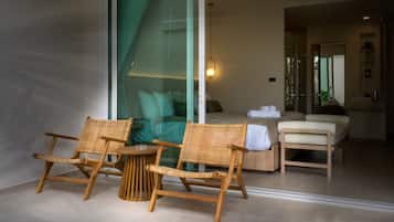 A modern room with a glass door leading to a balcony, a wooden chair, a small round table, and a sofa with a cushion.