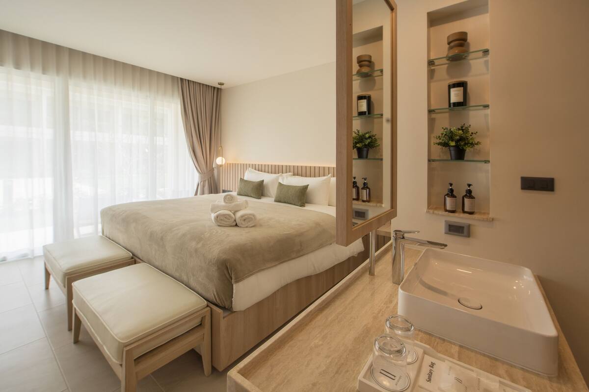 Una habitación de hotel moderna con una cama grande, una mesita de noche con un vaso, un estante empotrado con artículos de aseo y una bañera amplia.