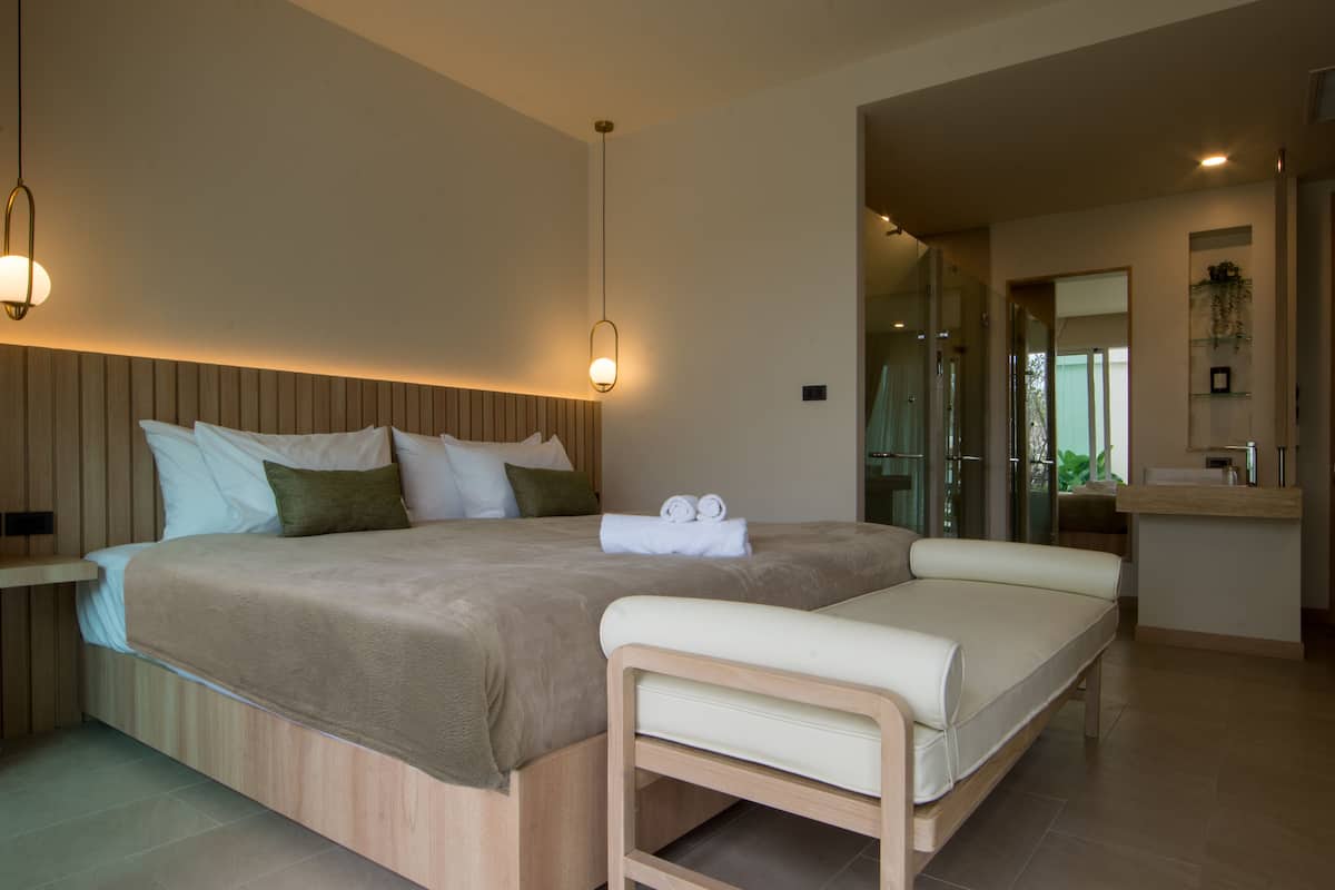 Un dormitorio moderno con una cama grande, mesitas de noche, un banco y una zona de baño con espejo y lavabo.