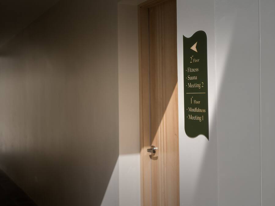 Un pasillo con un letrero que indica que el segundo piso tiene un gimnasio, sauna y la Sala de Reuniones 2, y el primer piso ofrece un espacio para la atención plena y la Sala de Reuniones 1.