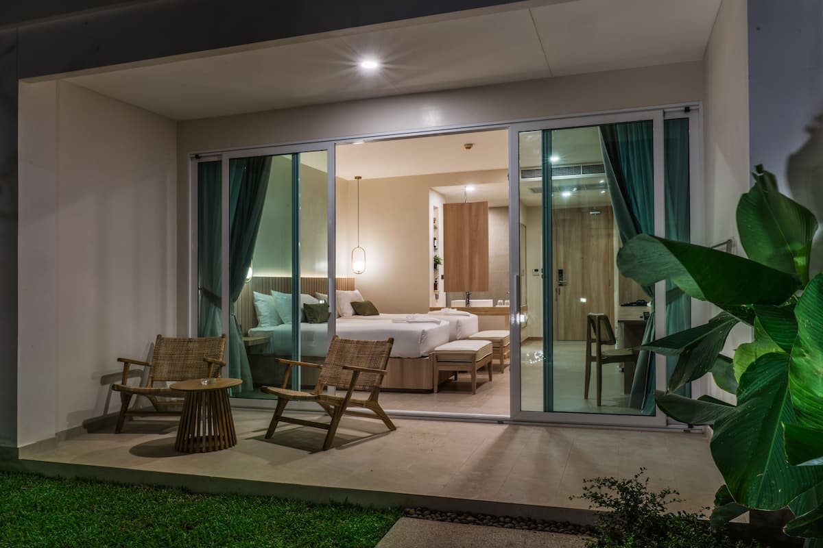 Habitación de hotel moderna con puerta de cristal que da a un balcón, amueblada con cama, dos sillas y una mesita.