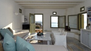 Een ruime kamer met een witte bank, een eettafel en uitzicht op zee.