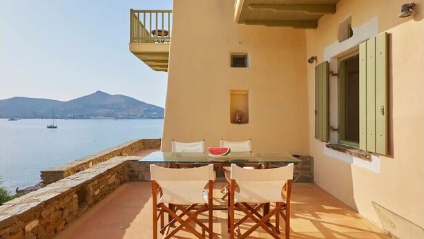 Een tafel met stoelen op een balkon met uitzicht op water en bergen.