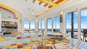 A vibrant, nautical-themed bar area with a colorful tiled floor, a stainless steel sink, and a view of the ocean through large windows.