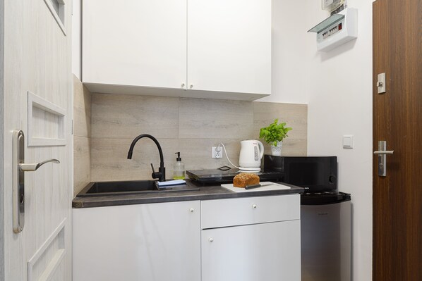 A compact kitchen with white cabinets, a black countertop, a coffee maker, a toaster, and a trash bin. - ShortStayPoland Tamka (Warsaw)