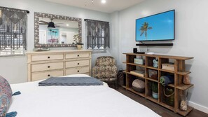 Un dormitorio con cama, cómoda, silla y televisor en la pared.