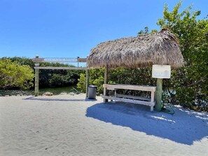 A beach area with a thatched structure, a wooden bench, and a signpost. - Sunshine Paradise Key Largo Ocean Pointe 4402 (Tavernier)