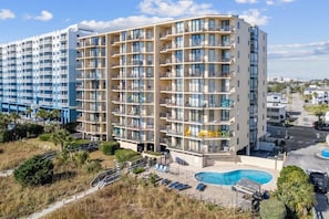 A multi-story hotel with balconies, a swimming pool, and a parking area.