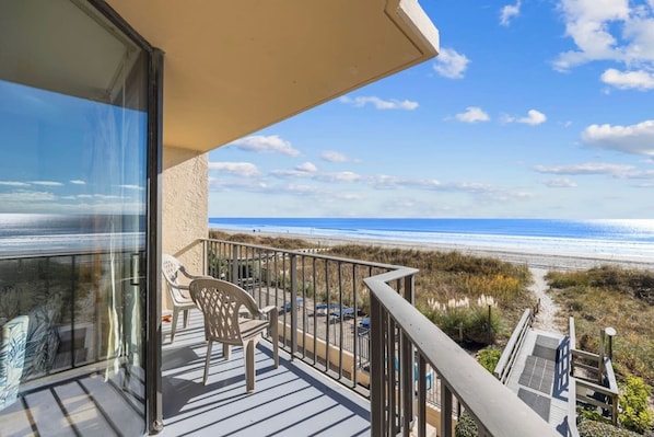 A balcony with a view of the beach, a chair, and a railing.
