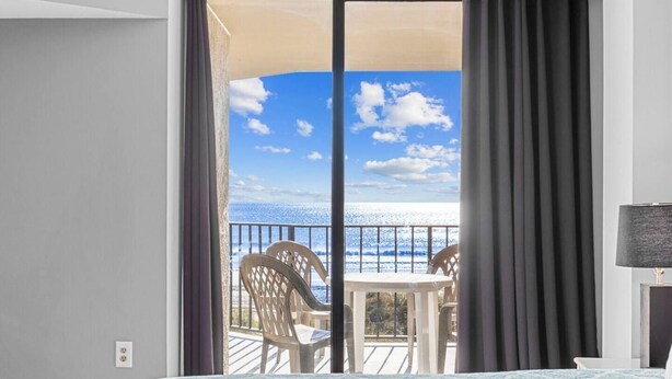 A hotel room with a balcony, a bed, a table, and chairs.