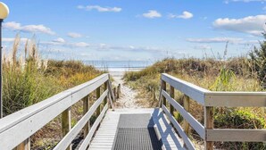 A wooden boardwalk leading to a beach with a clear sky.