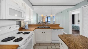 A modern kitchen with white cabinets, a wooden countertop, a built-in dishwasher, and a stove.