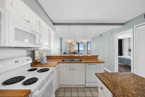A modern kitchen with white cabinets, a wooden countertop, a built-in dishwasher, and a stove. - Oceanfront Summit Bliss 3 BR w/ balcony (North Myrtle Beach)