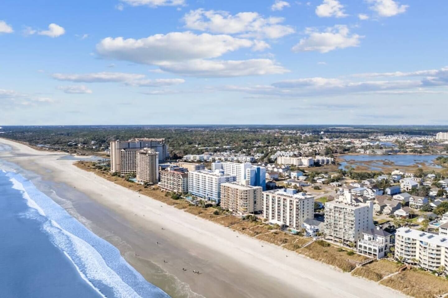 A coastal cityscape with beachfront hotels, a sandy beach, and a clear sky.