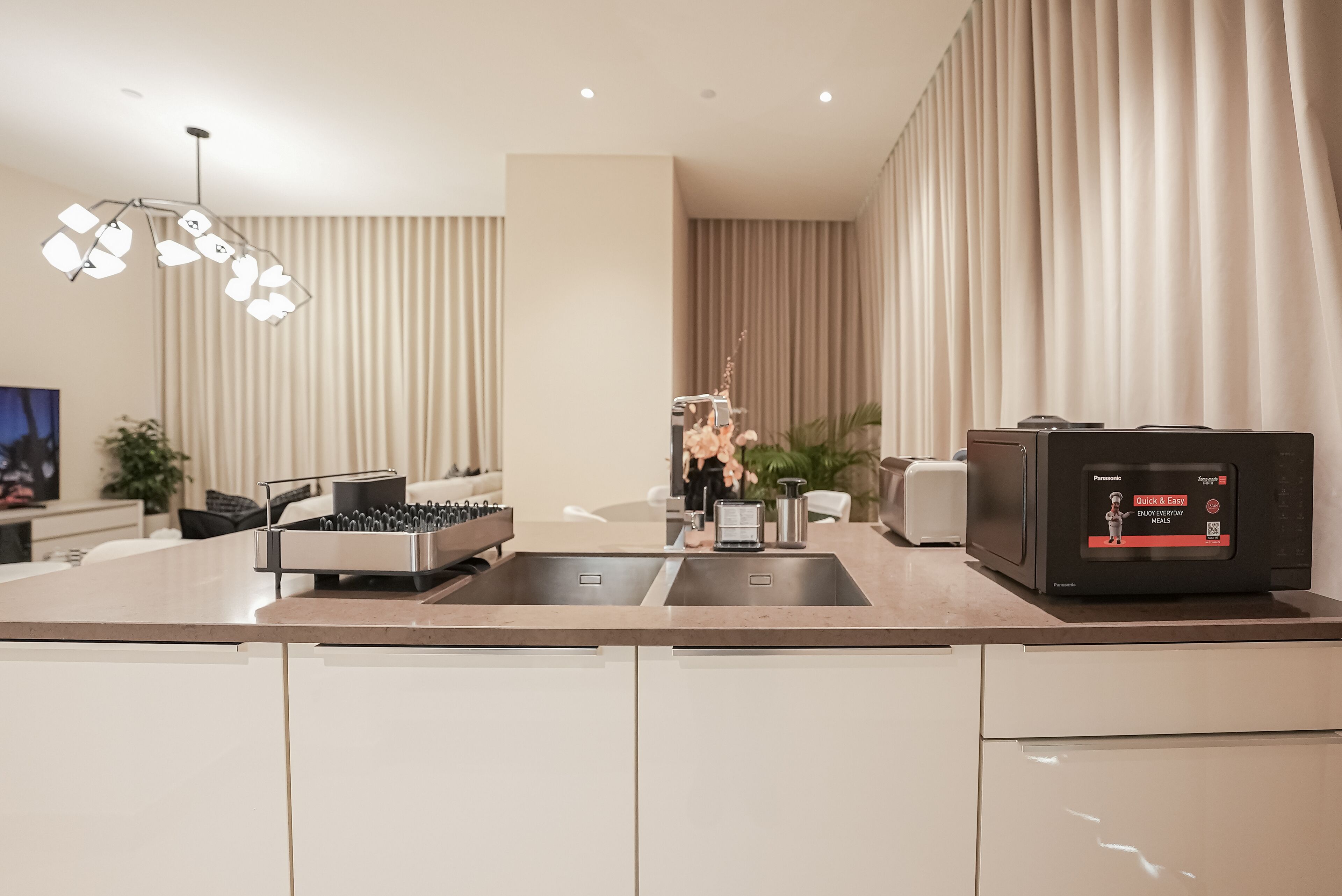 A modern kitchen with a built-in dishwasher, a coffee machine, and a large window with curtains.