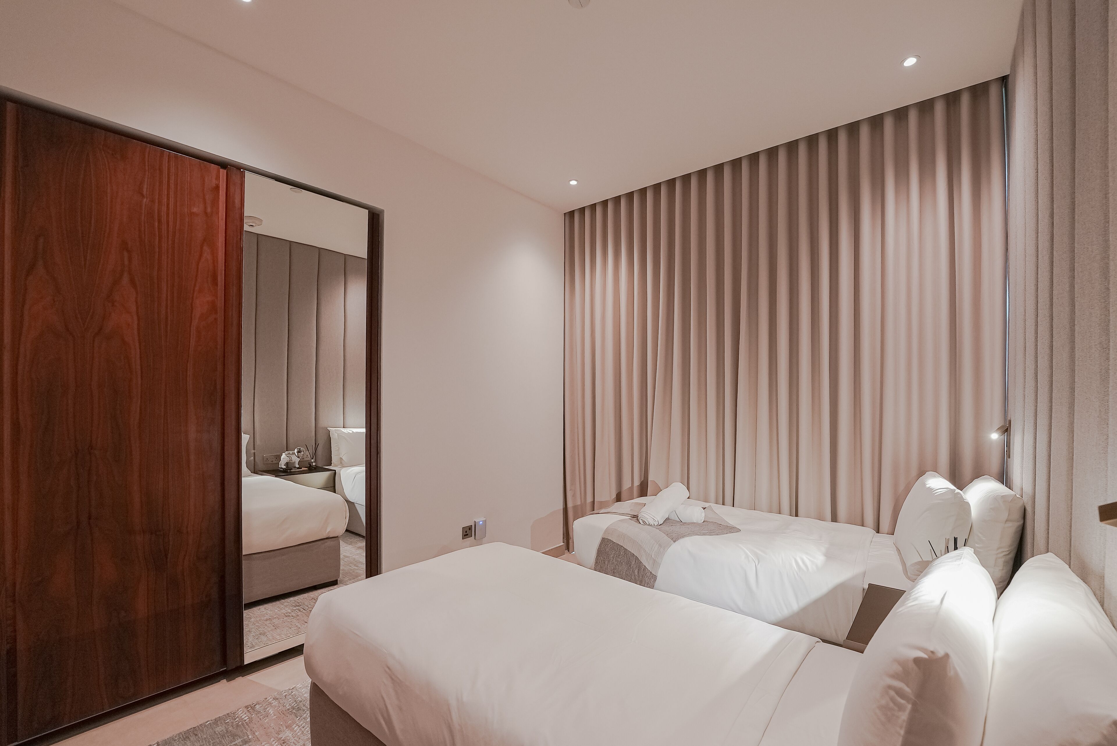 A modern hotel room with two beds, a large mirror, and a sliding door.