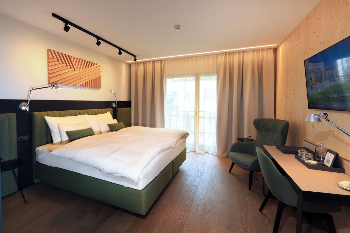 A modern hotel room with a large bed, a desk, a chair, and a TV.