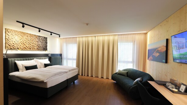 Une chambre d’hôtel avec un lit, un canapé, un bureau avec une chaise et un téléviseur fixé au mur.