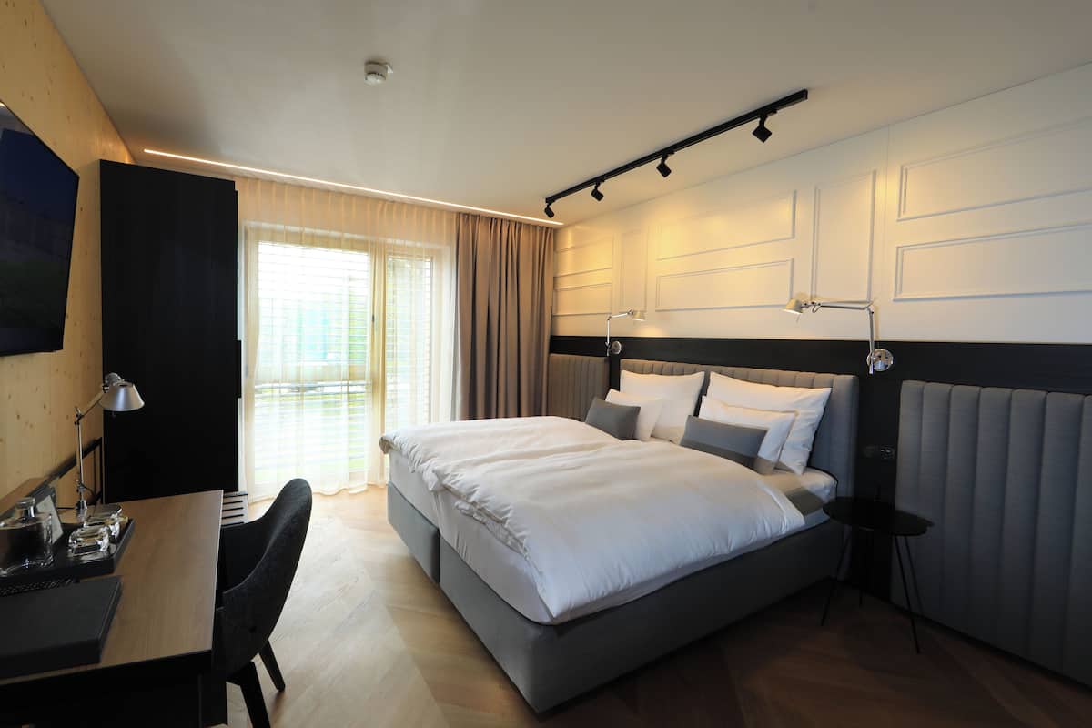 A modern hotel room with a large bed, a desk with a chair, and a small table.