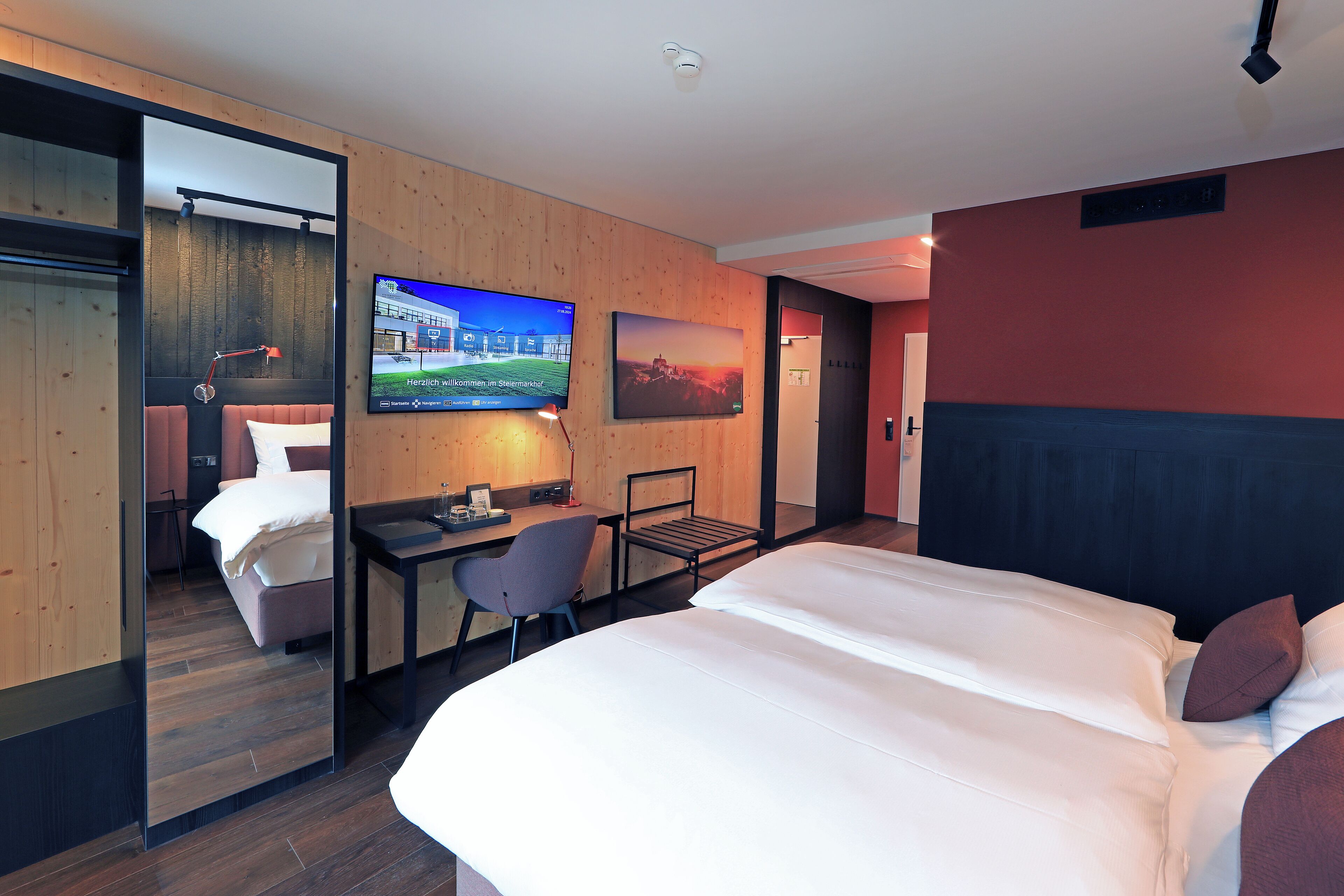 Una habitación de hotel moderna con una cama grande, un escritorio, una silla, un televisor y un cuadro en la pared.