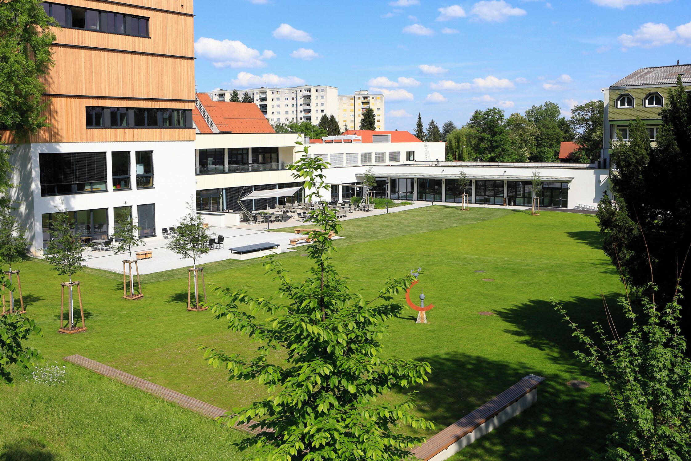 Ein modernes Gebäude mit Innenhof, Außenbestuhlung und einem großen Rasen.