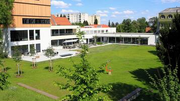 Ein modernes Gebäude mit Innenhof, Außenbestuhlung und einem großen Rasen.