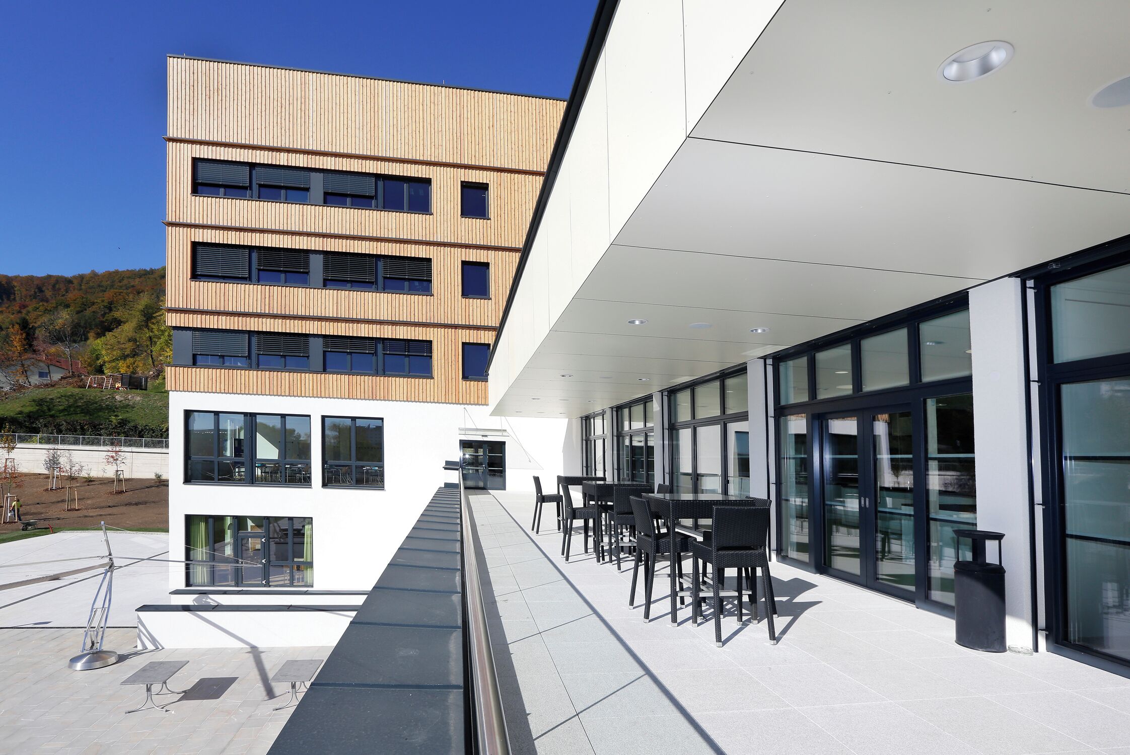 A modern building with a flat roof, large windows, and outdoor seating area.