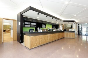 Un área de recepción moderna con mostrador de madera, pared verde e iluminación empotrada en el techo.