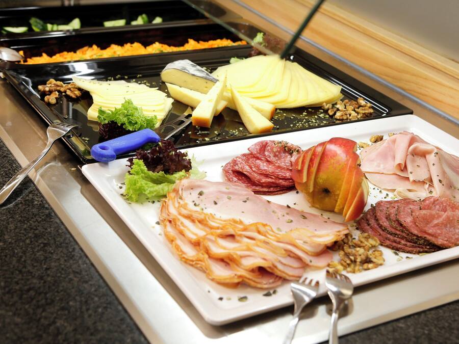 Un bufé con una variedad de alimentos, entre ellos queso, jamón y frutas.