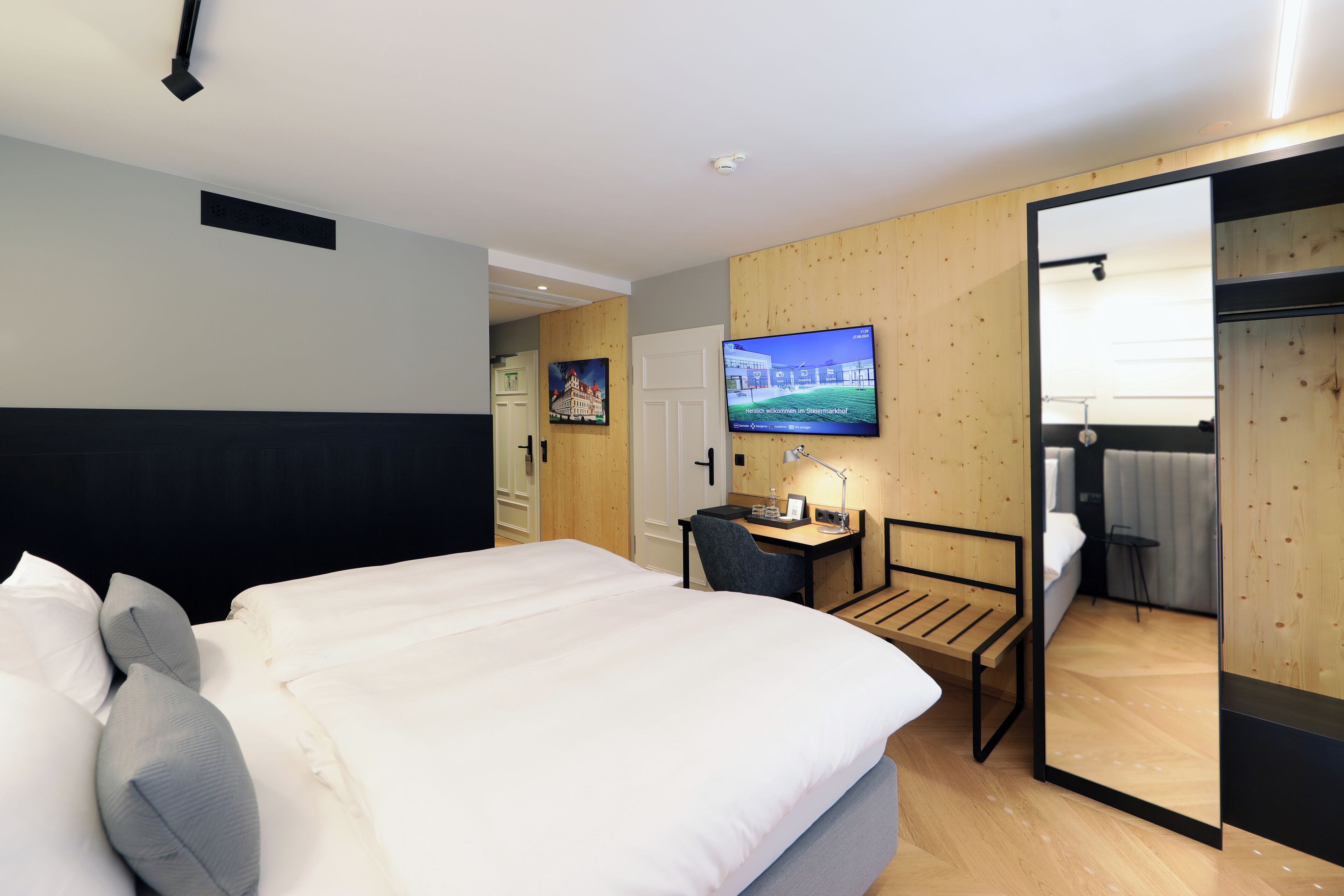 Une chambre d’hôtel avec un grand lit, un bureau, une chaise, une télévision et un miroir.
