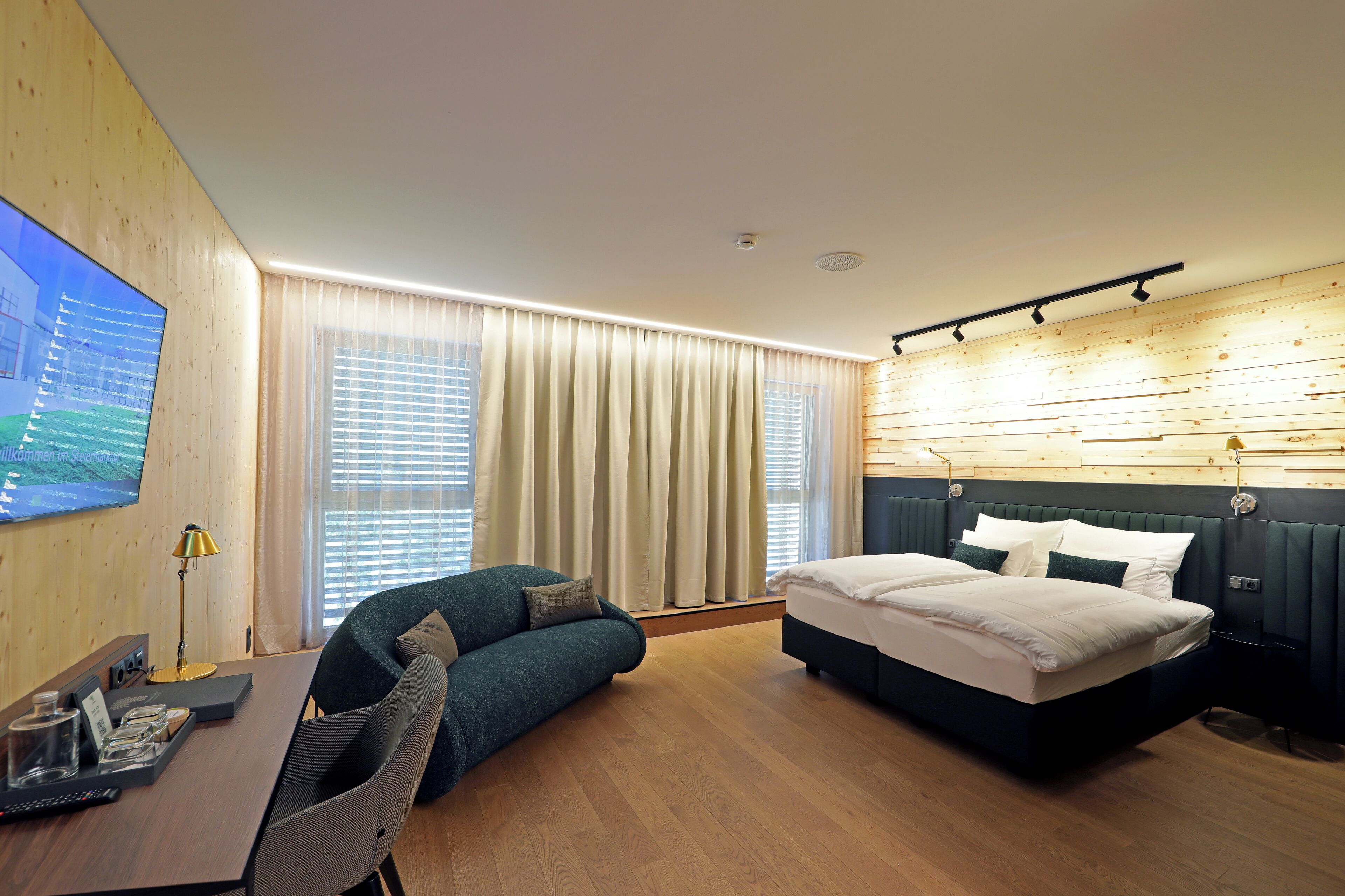 Een moderne hotelkamer met een houten vloer, een groot bed, een bank, een bureau met lamp en een televisie aan de muur.