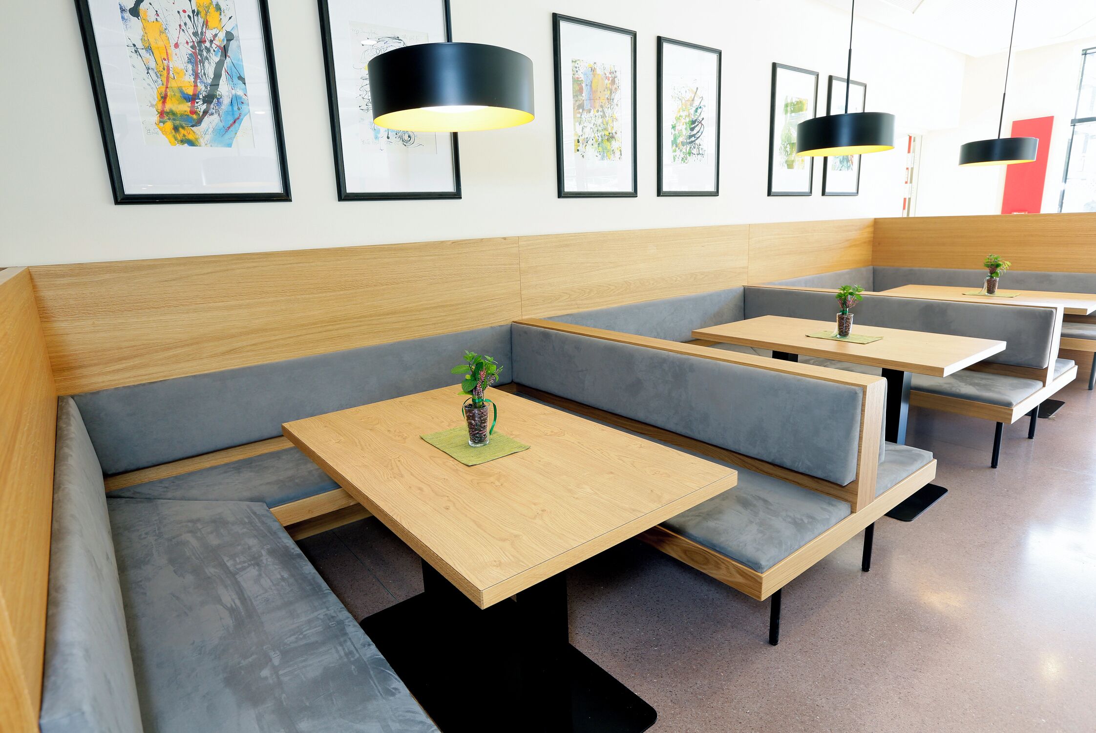 A modern restaurant with grey cushioned booths, wooden tables, and black pendant lighting.
