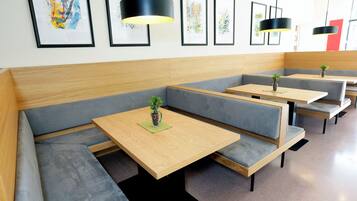 A modern restaurant with grey cushioned booths, wooden tables, and black pendant lighting.