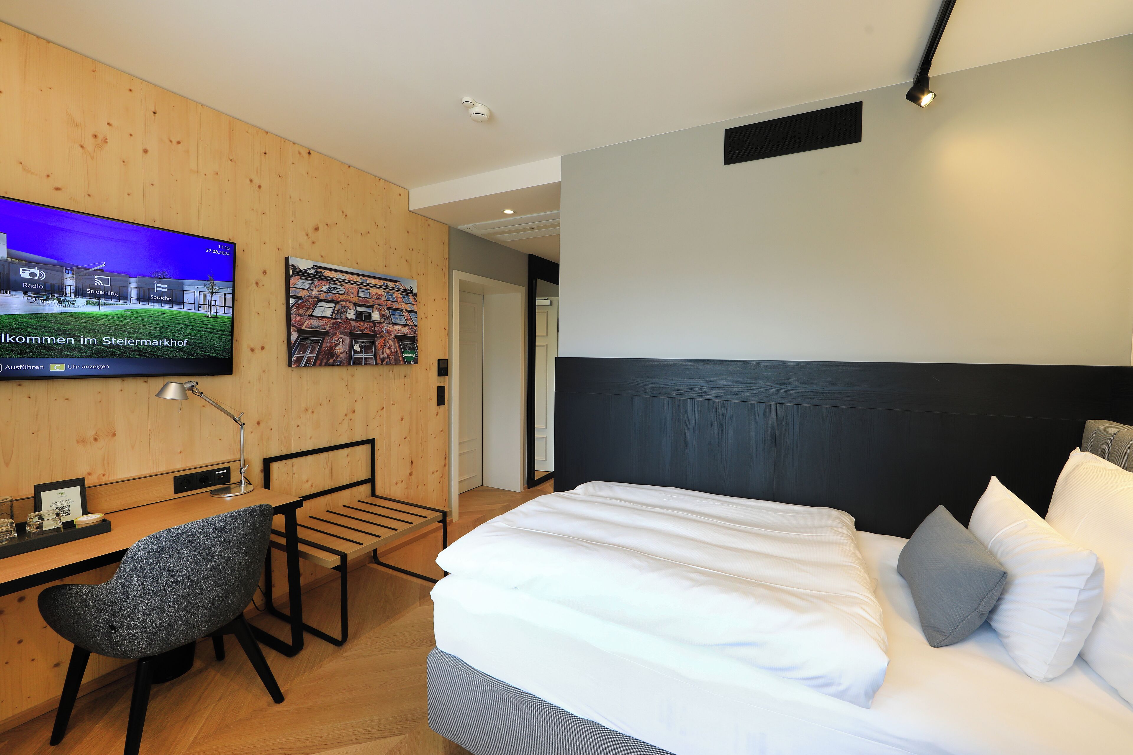 Habitación de hotel moderna con cama, escritorio, silla, televisor y un cuadro en la pared.