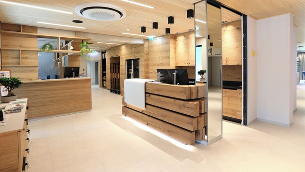 A modern reception area with wooden reception desk, built-in shelving, and a large mirror. - Hotel Steiermarkhof (Graz)