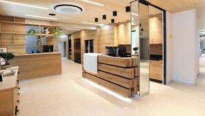 Un espace d’accueil moderne avec un comptoir de réception en bois, des étagères intégrées et un grand miroir.