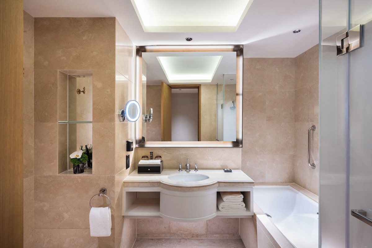 A modern bathroom with a skylight, a large mirror, a sink, a bathtub, and a glass shower enclosure.