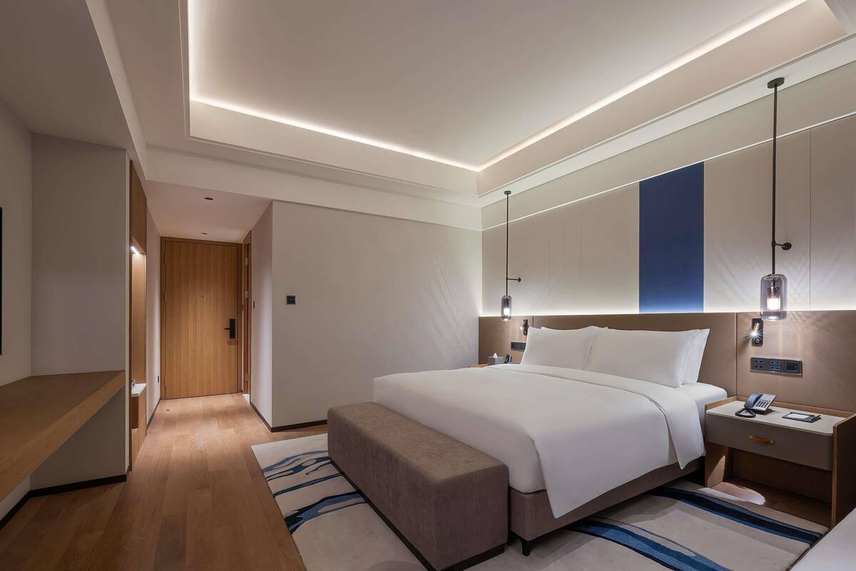A modern hotel room with a large bed, bedside tables, a desk, and a mirror.